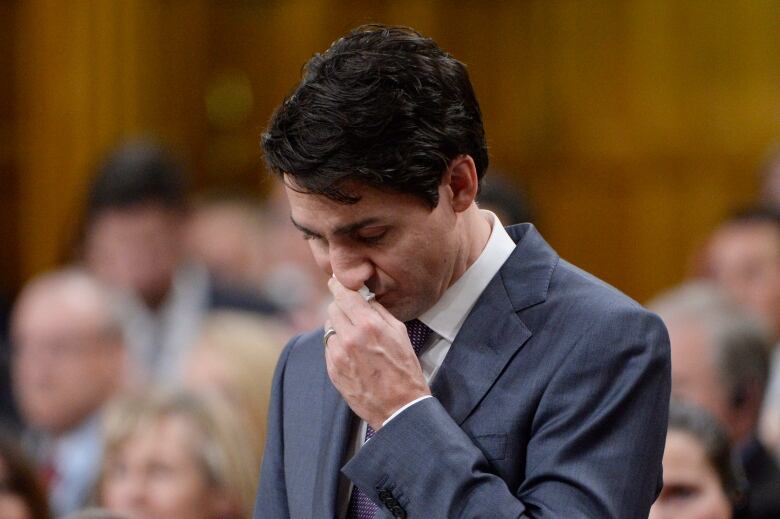 A man looks down, holding a Kleenex to his nose.