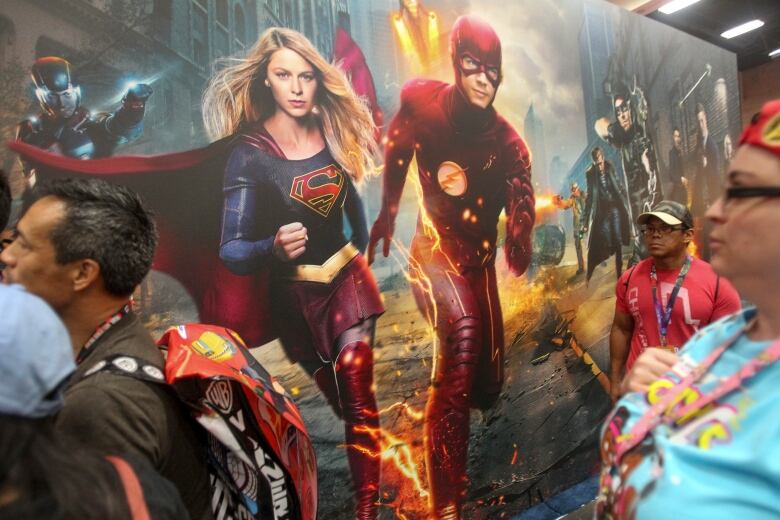 Convention-goers saunter by as Supergirl and The Flash jump pff a mural during Comic-Con International 2016 in San Diego, California on July 21, 2016. 