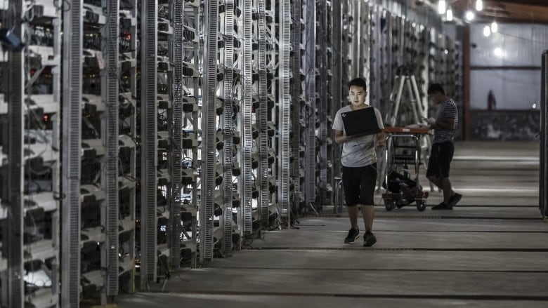 A person with a laptop walks beside a row of floor-to-ceiling computer servers.