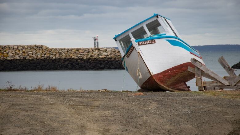 A small boat is shown tilting on it side on the ground.