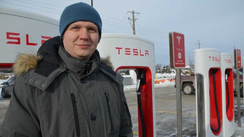 A man wearing winter clothing standing in front of a Tesla fast charging system.