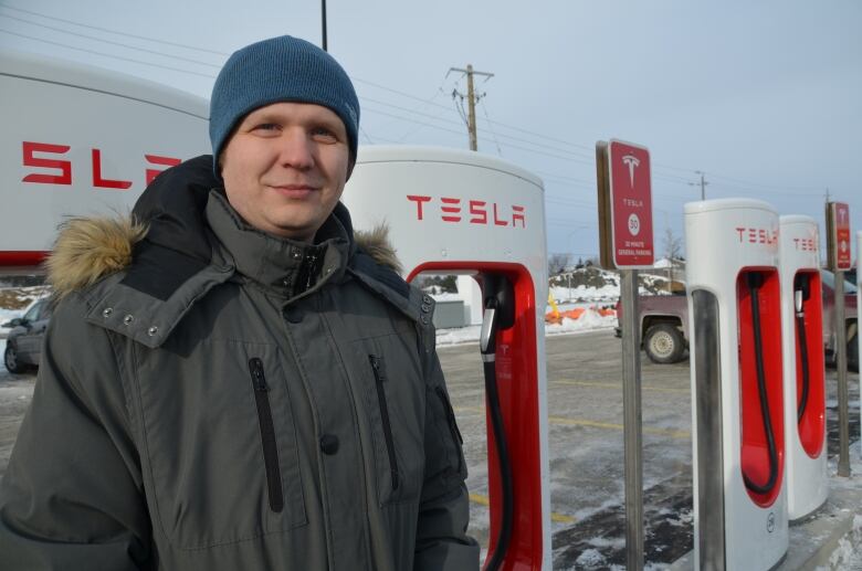 A man wearing winter clothing standing in front of a Tesla fast charging system.