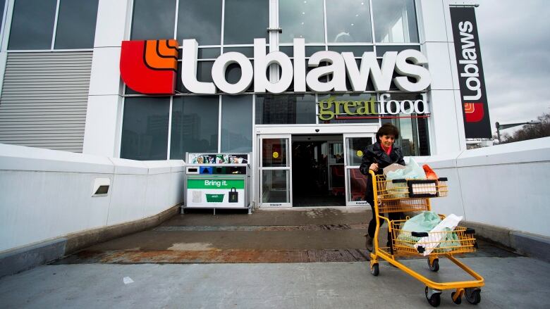 A woman pushes a shopping cart out of Loblaws.