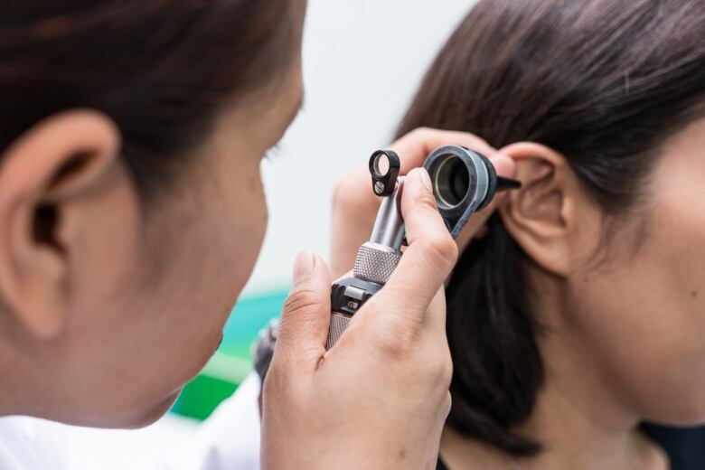 A male doctor examines a woman's ear with an otoscope. 