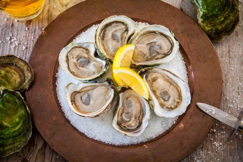 A half dozen oysters sits on a bed of ice with slices of lemon.