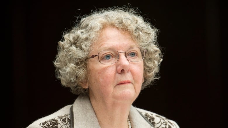 A woman in a blazer and pearl necklace sits at a desk.