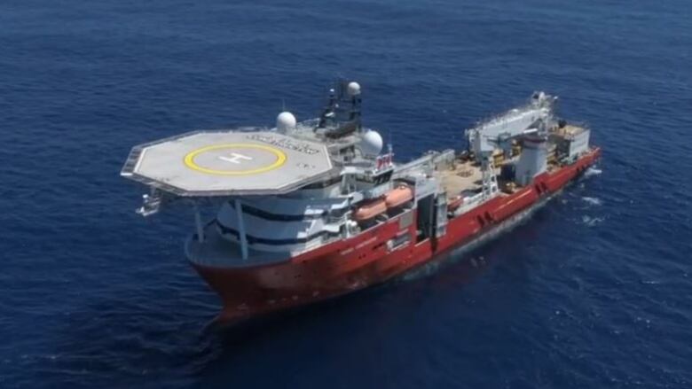 A large ship with a helicopter landing pad is shown at sea.