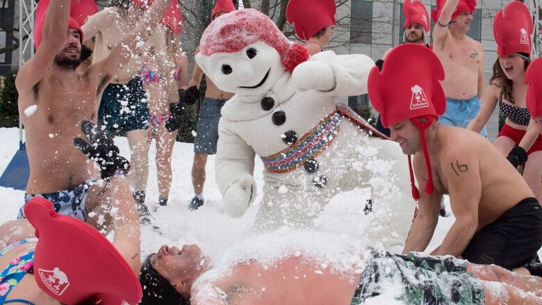 People in bathing suits rolling in the snow. 