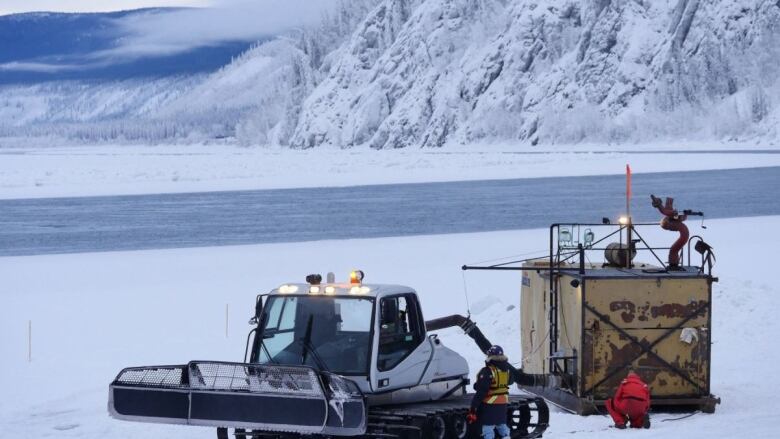 Machinery and construction workers beside a a snowy stretch of river. 