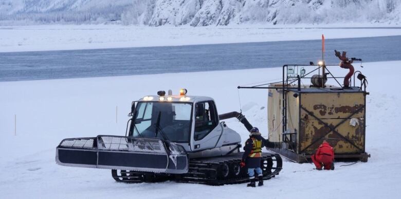 Machinery and construction workers beside a a snowy stretch of river. 