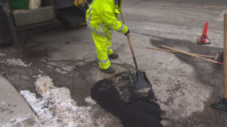 Person in a yellow neon work suit patches a pothole