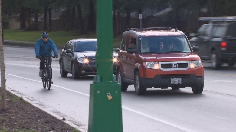 A cyclist in blue jacket rides in a bike lane without any barriers next to traffic