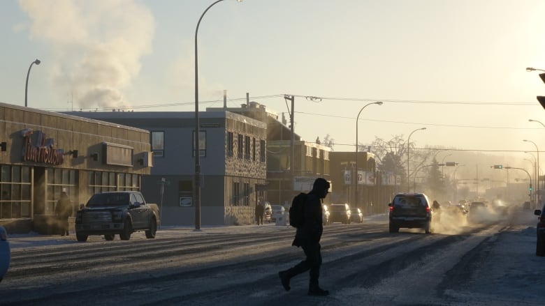 A person crosses a busy street in downtown Whitehorse during winter as the sun sets