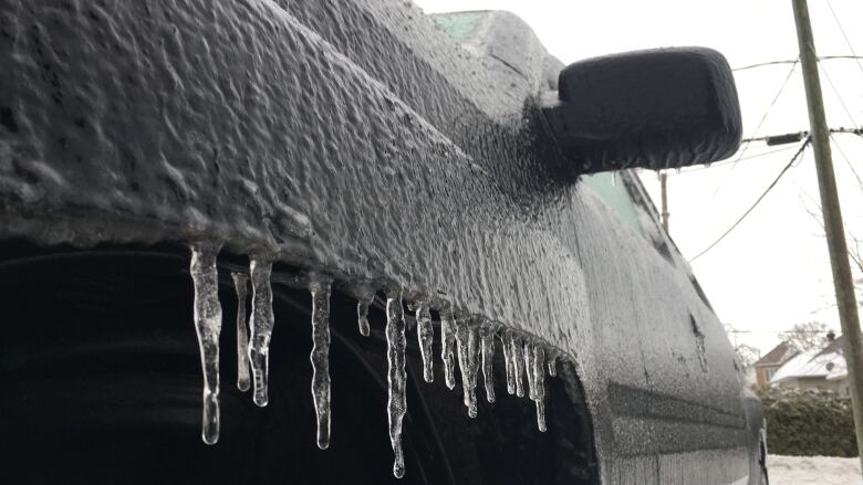 A vehicle coated in ice has small icicles hanging from a front wheel well.