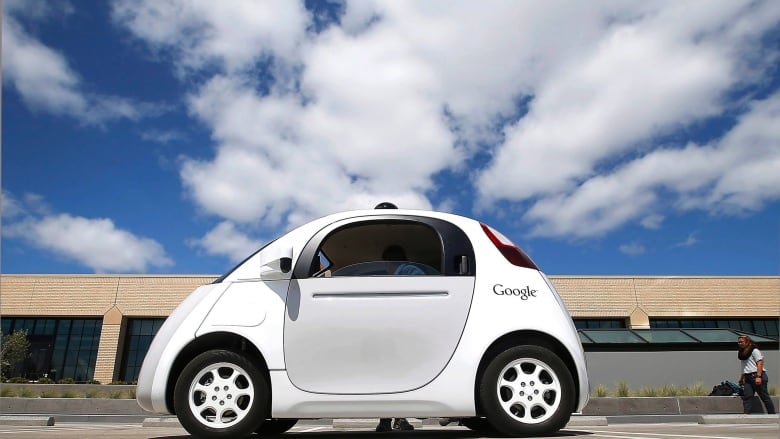 A two-door white car with a Google decal is parked in front of a low-rise building