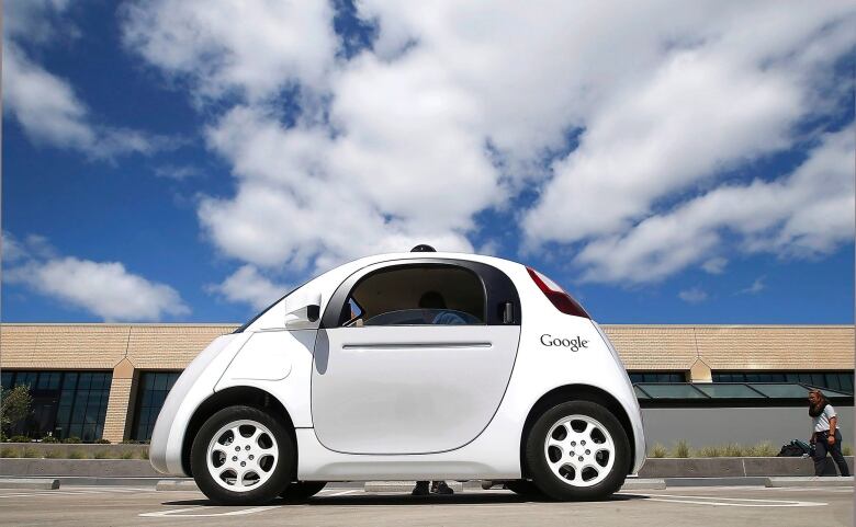 A two-door white car with a Google decal is parked in front of a low-rise building