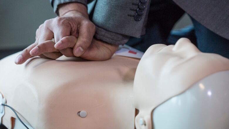 Hands perform chest compressions on a dummy.