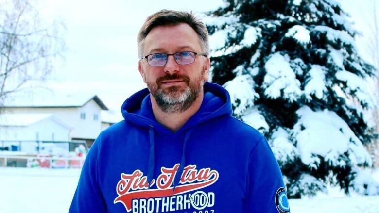 Man in glasses stands outside in hoodie.