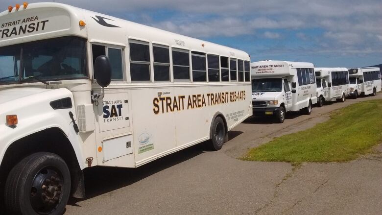 A lineup of white vans and a bus is shown.