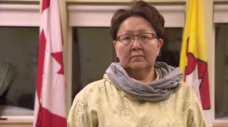 A woman wearing yellow Inuit clothing standing in front of two flags