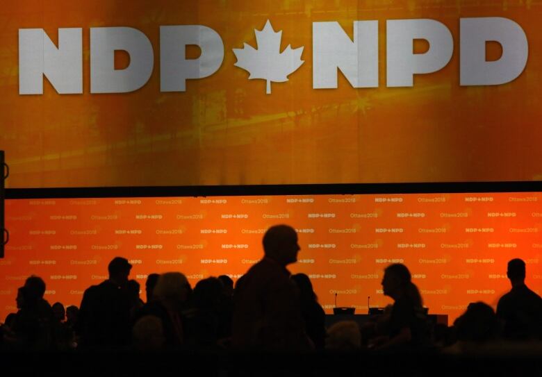 People stand in front of an orange NDP banner.