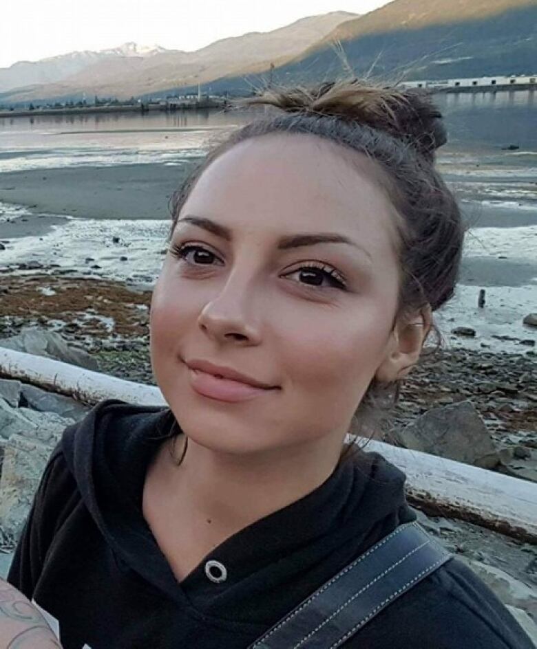 A young woman with her hair tied in a bun takes a selfie.