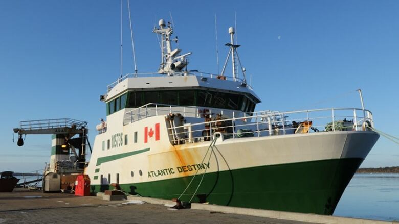 A large green and white trawling ship at dock.