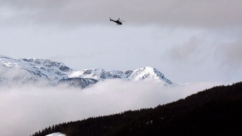 A helicopter flies over a snow-capped mountain.