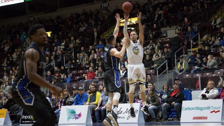 A basketball player takes a jump shot as another leaps forward to block him.