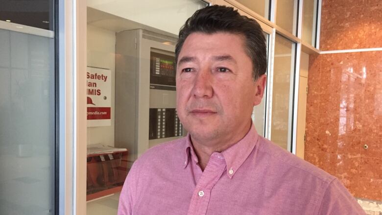 An Indigenous man with short hair is seen wearing a pink button up shirt.