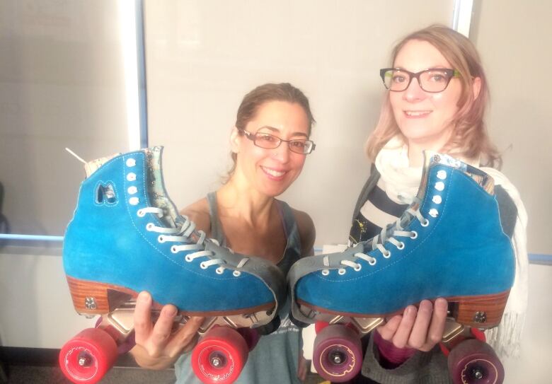 Two women each hold a skate. 