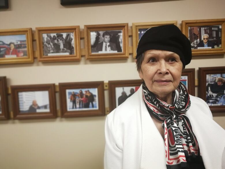 A woman stands in front of a wall of portraits.