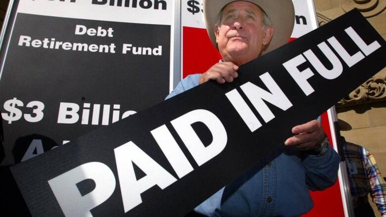 a man in a cowboy hat holds a sign saying 'paid in full' 