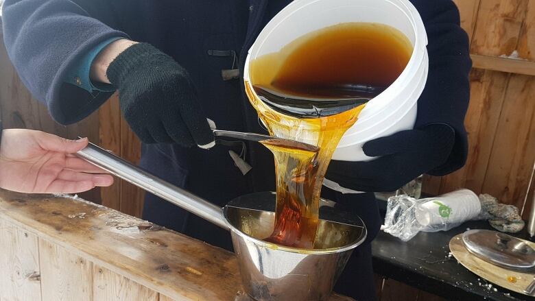 A bucket of maple syrup being poured from a white bucket into a metal bucket.