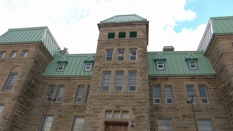 A low-angle view of a large stone building with a green metal roof.