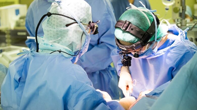 Doctors wearing medical scrubs are shown inside of a hospital room.