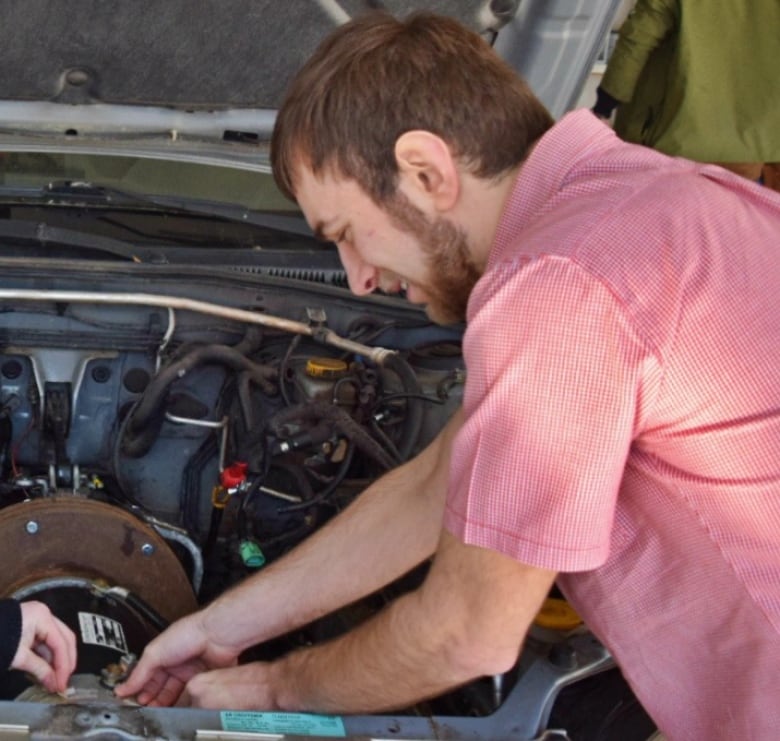 Two men with their hands in the hood of a car