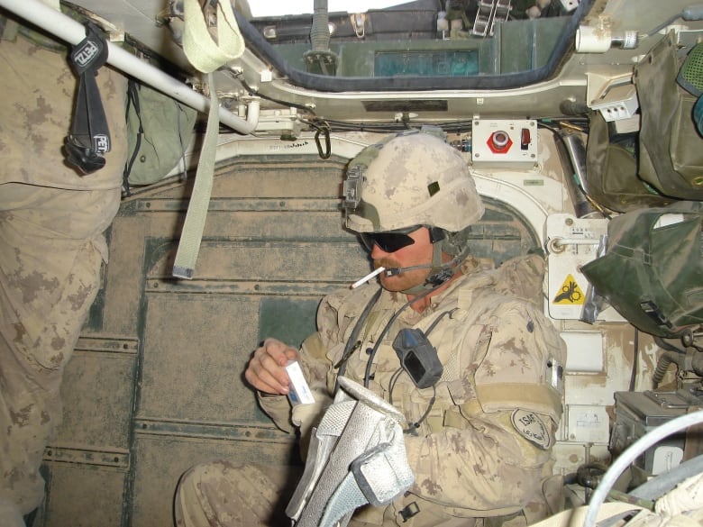 A man in army fatigues and helnet, inside a tank.