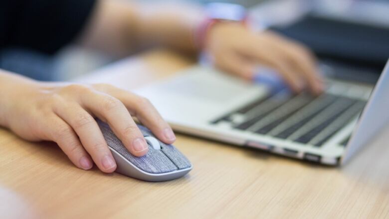 Stock image of hand on mouse next to keyboard.