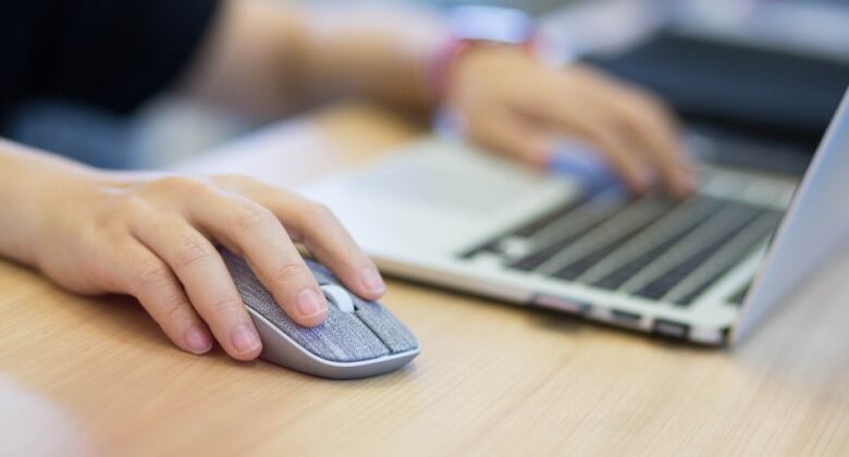 Stock image of hand on mouse next to keyboard.