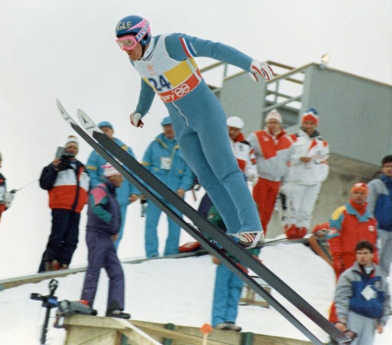 A man in  a blue outfit takes part in a ski jumping competition