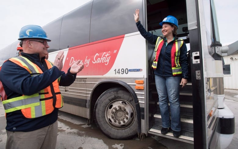 A man wearing a high-vis vest claps as a woman exits a bus.