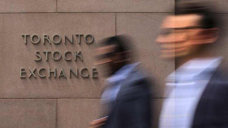 Two male figures walk past a TSX sign in downtown Toronto