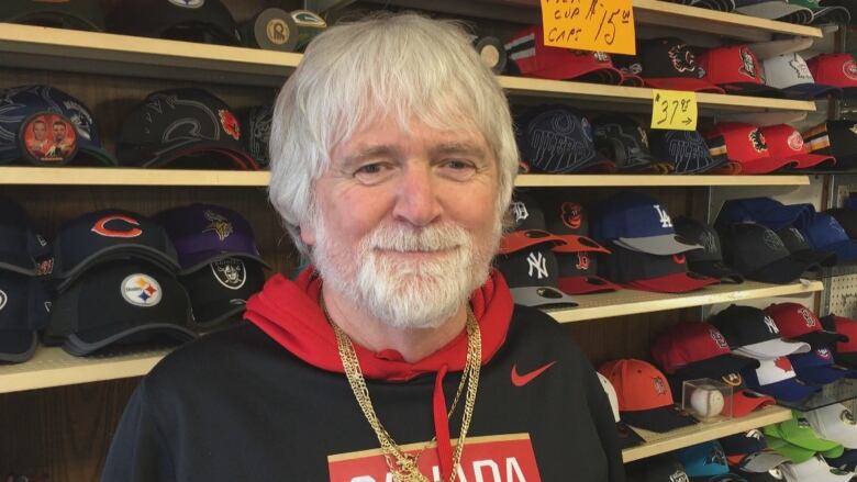 A man standing in front of a lot of baseball hats featuring different sports teams.