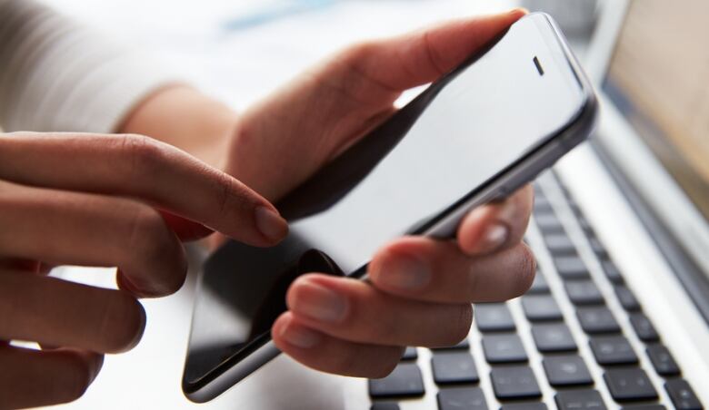 Person holding cell phone over a keyboard.