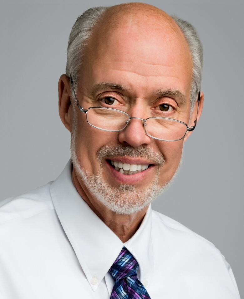 A man with glasses and a tie smiles.