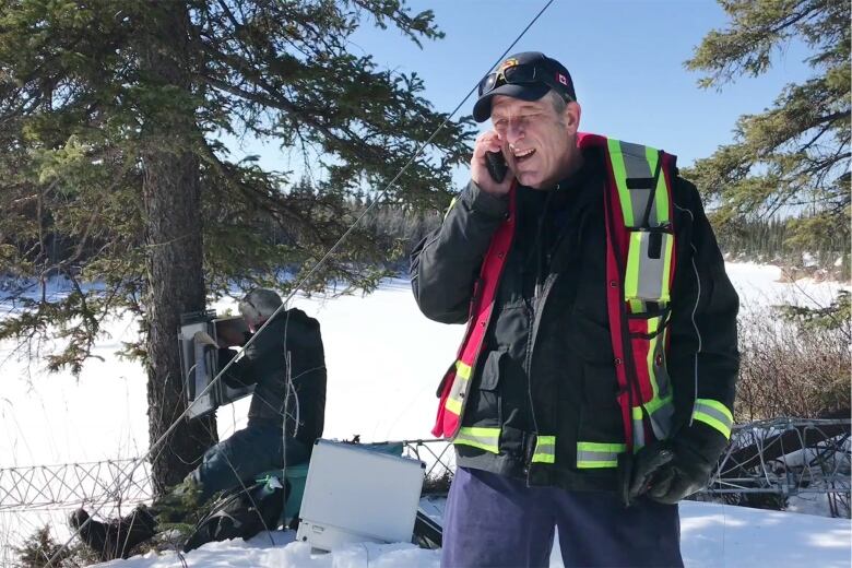 A man in a vest holds a phone up.