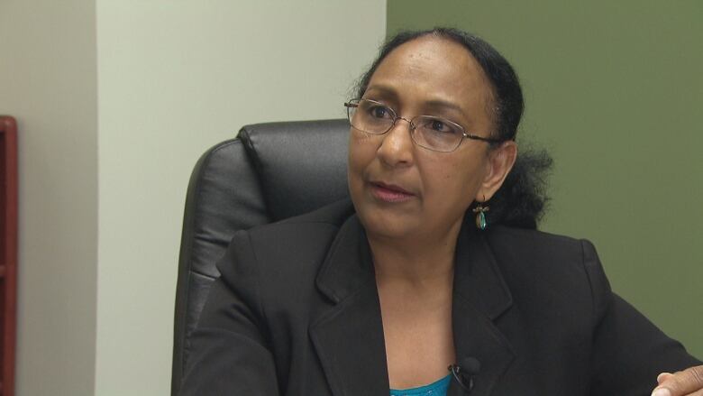 A woman wearing glasses and a black blazer looks to her left.