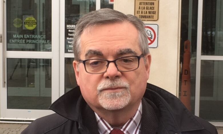 A man stares at the camera outside the courthouse, with microphones in front of him.