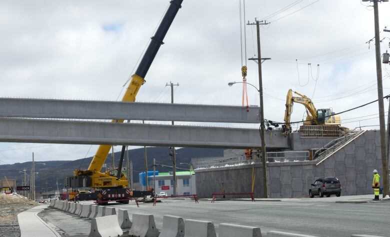 A crane lifts a concrete span into place at an overpass above Topsail Road.